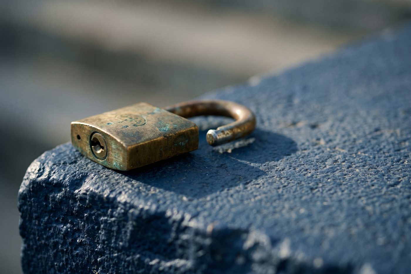 A heavy brass padlock resting open on a navy stone ledge, cool teal rim light, long shadow
