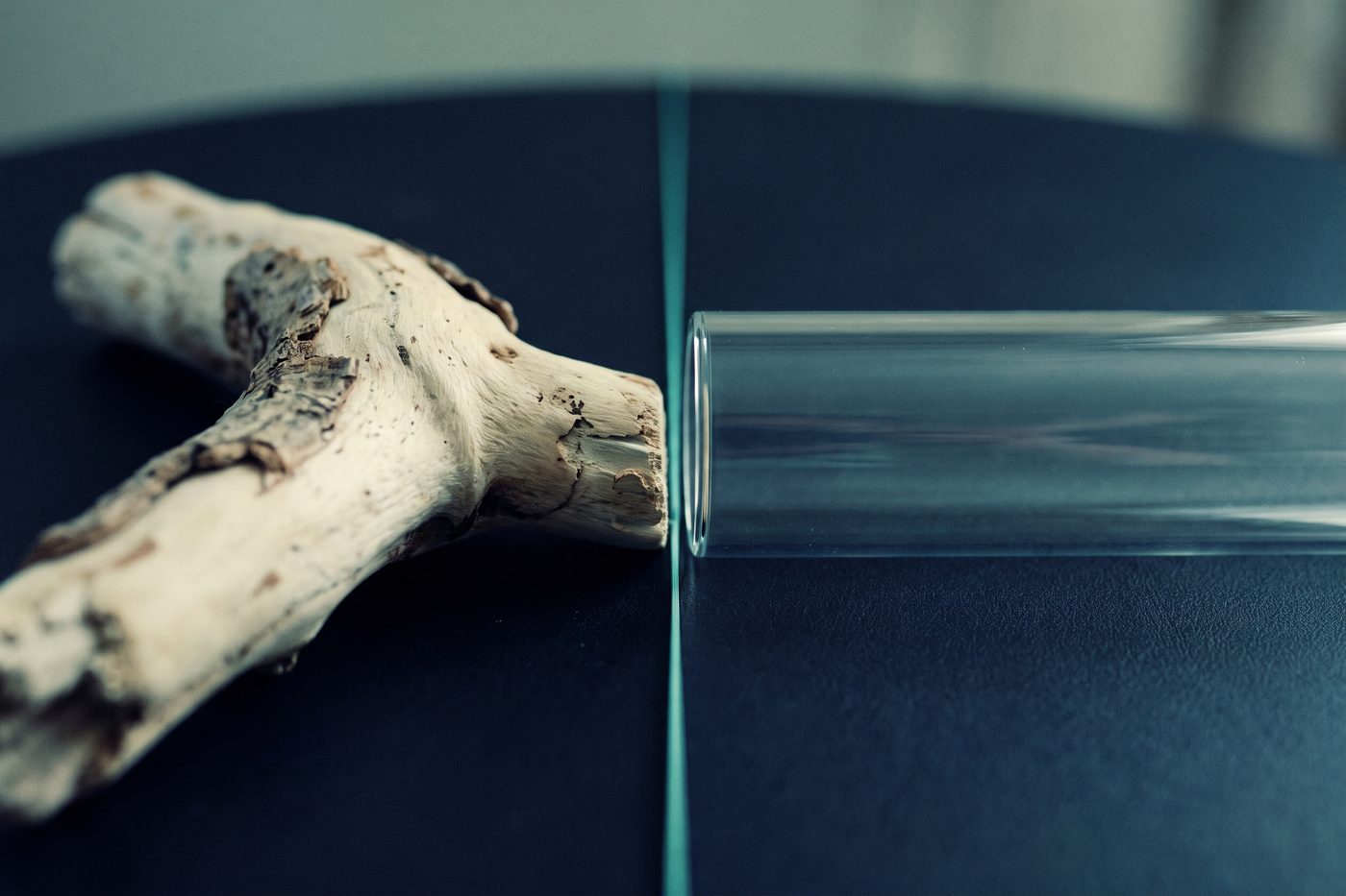 Weathered organic driftwood on the left, a flawless machined glass cylinder on the right