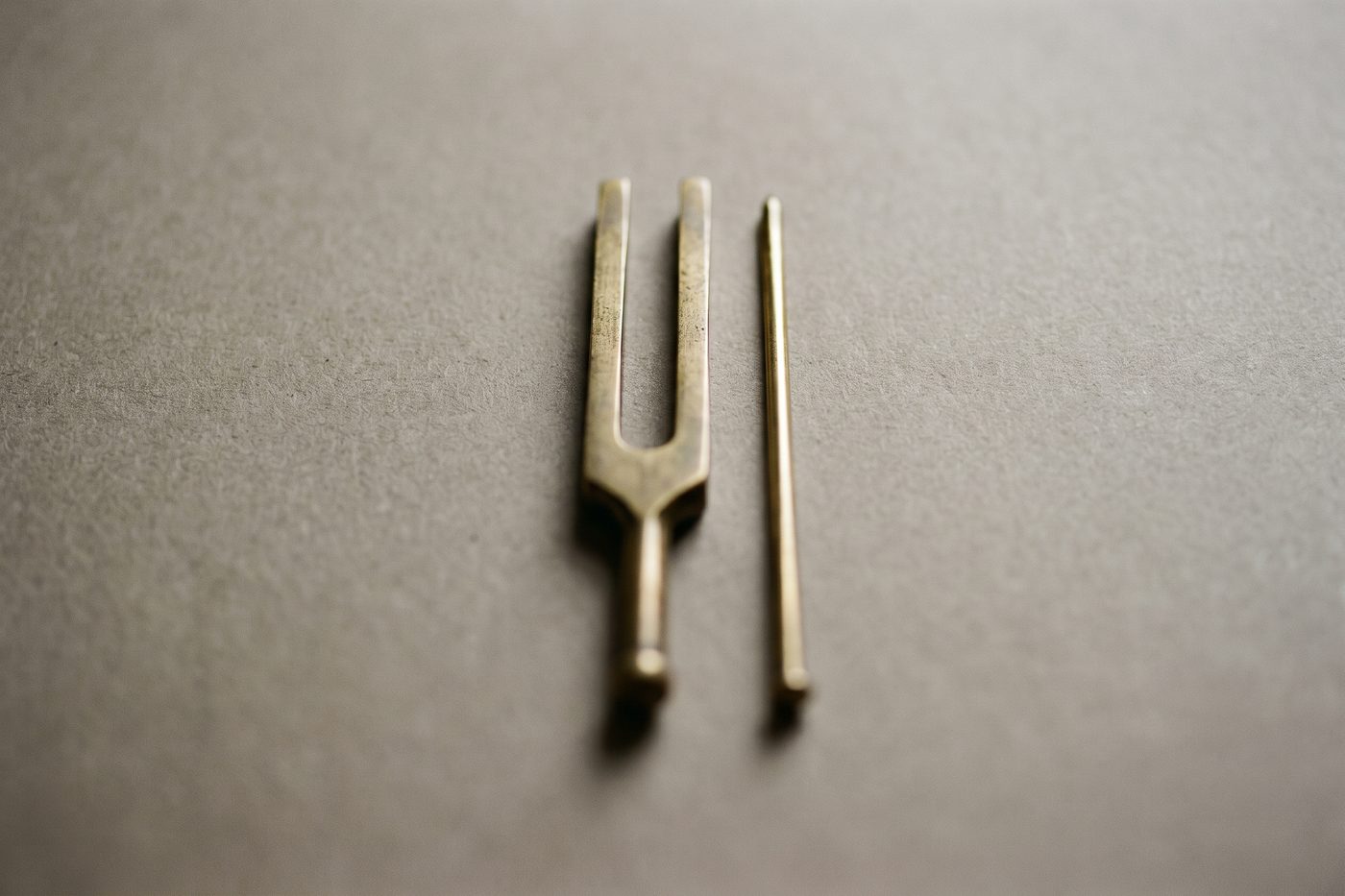 A brass tuning fork beside a fine brass pin on navy slate, symmetrical cool light