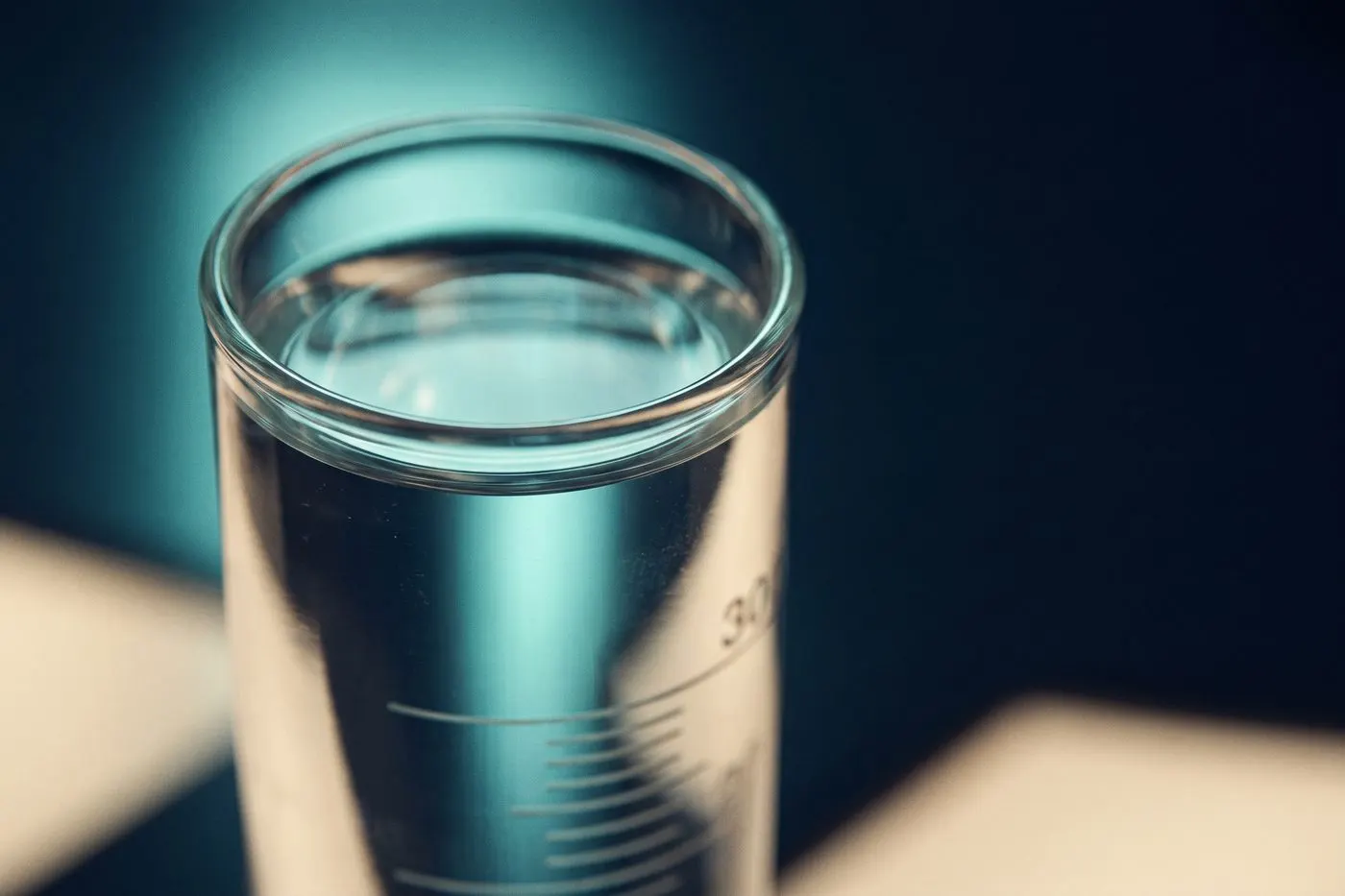 A graduated glass cylinder filled to a precise line, extreme macro on the curve of the meniscus, teal backlight, navy