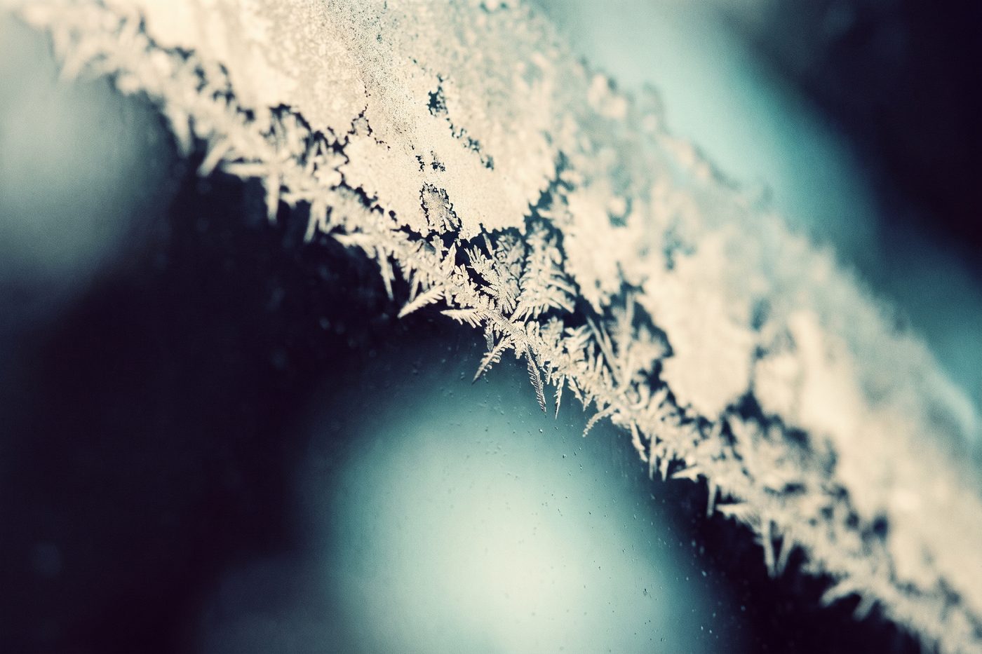 Frost crystals spreading across the inside of a glass panel with a cool teal glow behind, extreme macro, navy shadow