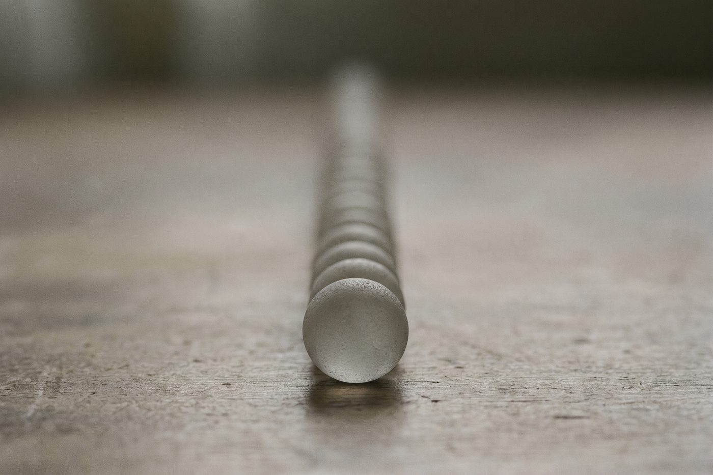 A line of identical frosted glass beads receding into deep navy shadow, the nearest sharply lit, the farthest almost lost