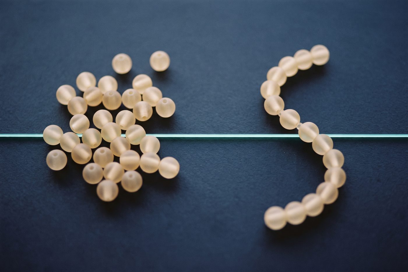 A scattering of loose frosted glass beads on the left and a single assembled strand of the same beads on the right