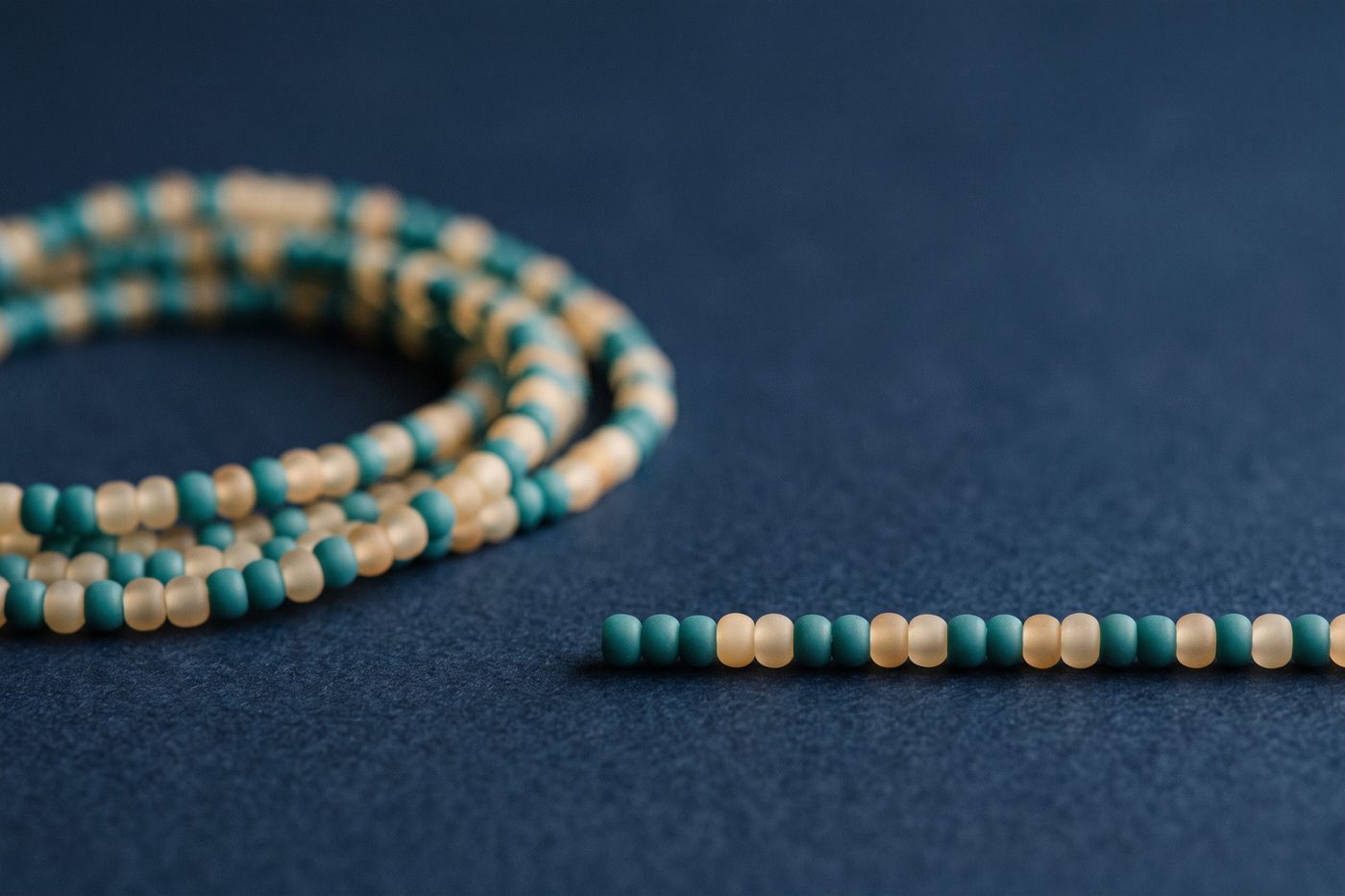 A short strand of frosted beads beside a long coiled strand of the same beads on navy, strong scale contrast