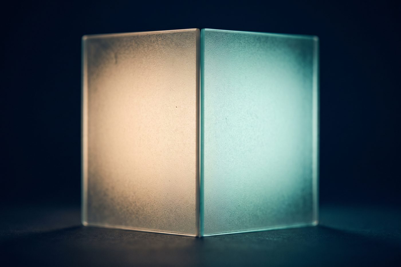 Two frosted glass panels side by side on navy, one lit warm amber and one lit cool teal, a sharp seam dividing them