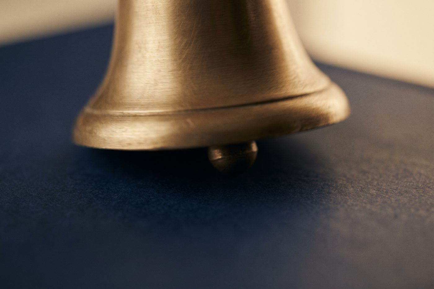 A struck brass bell with fine vibration blur at its rim, matte navy backdrop, cool directional light