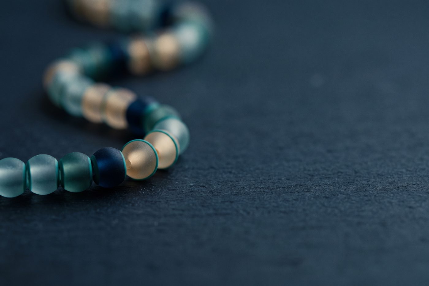 A delicate chain of small frosted glass beads resting on a matte deep-navy stone surface