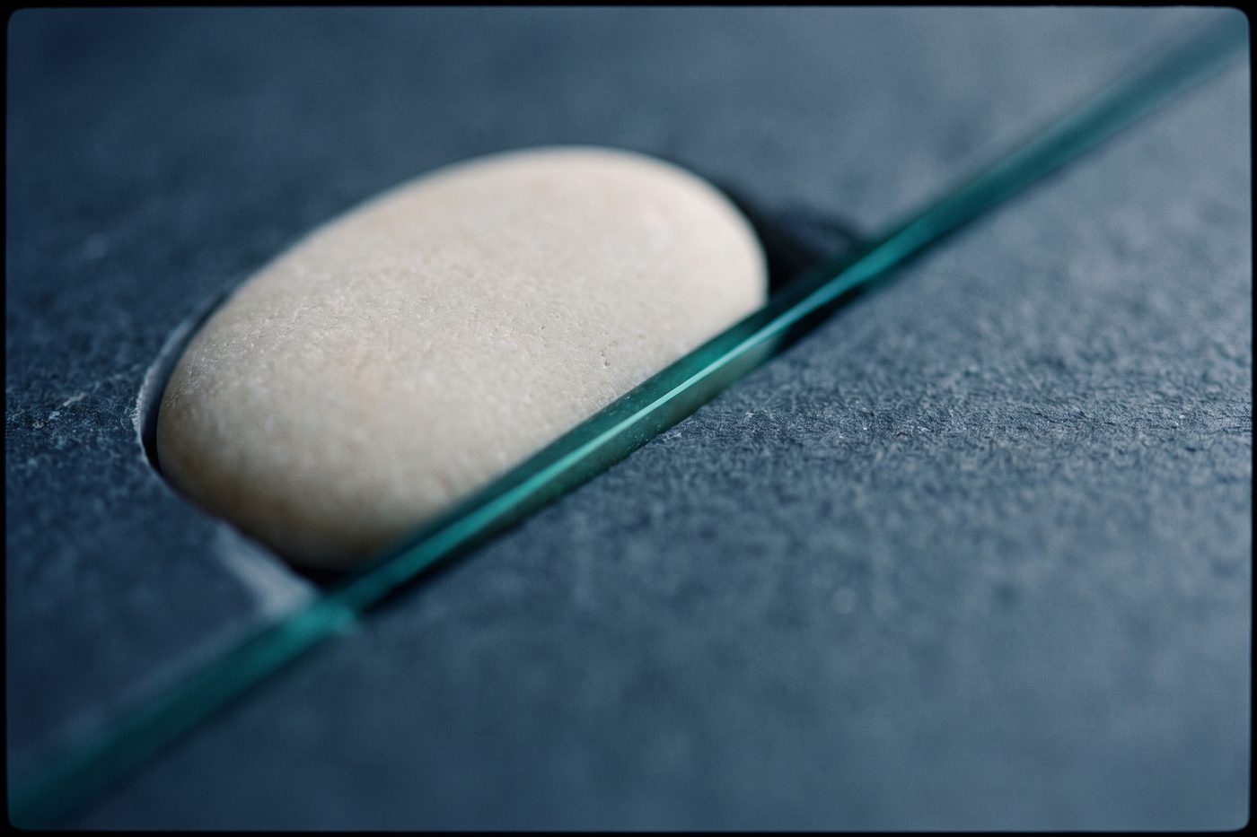 A smooth pale stone fitting exactly into a carved recess in a slab of navy slate, the join lit by a thin seam of teal light