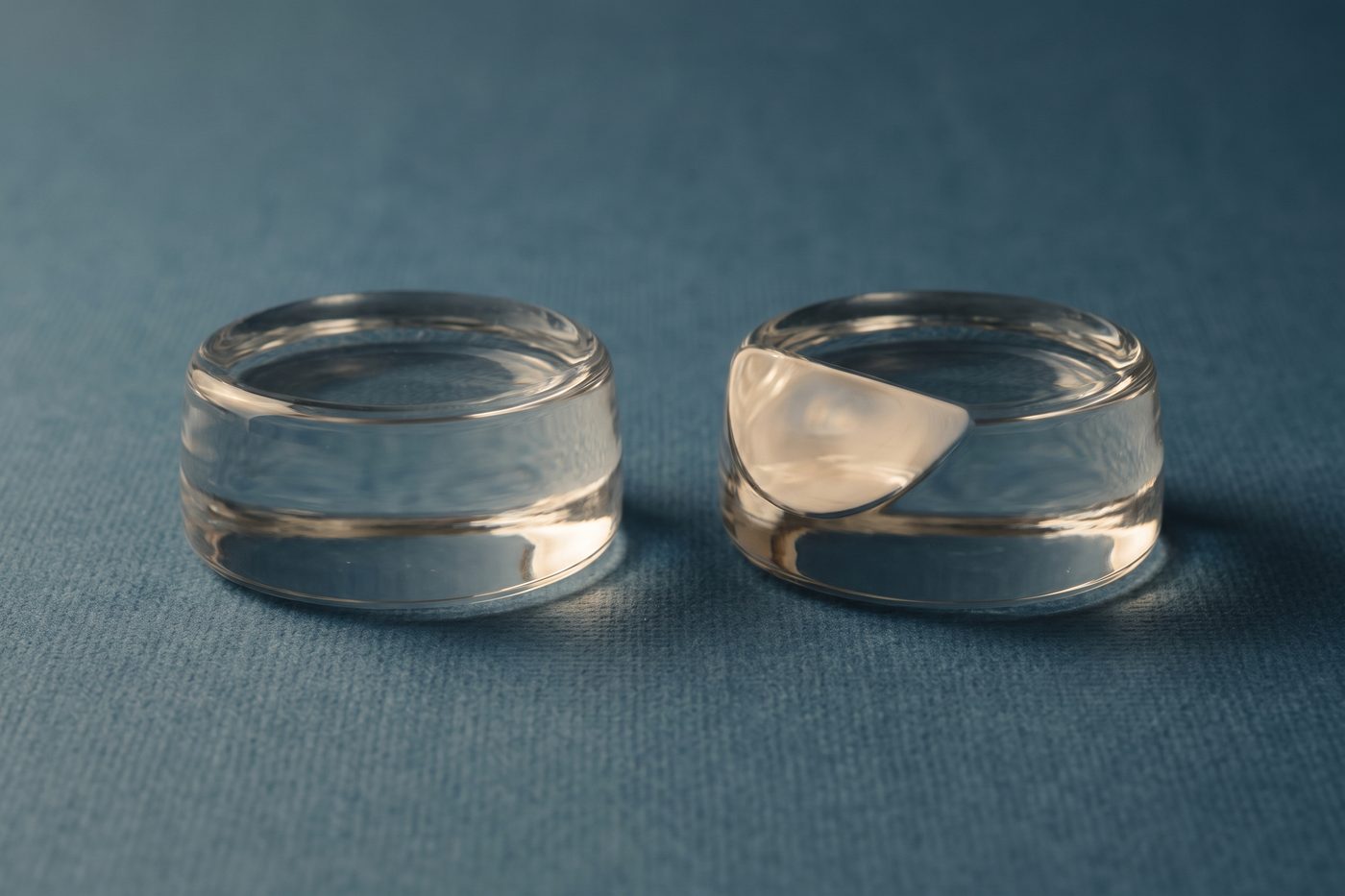 Two near identical cast glass forms side by side, one with a single facet subtly different, raking light across navy slate