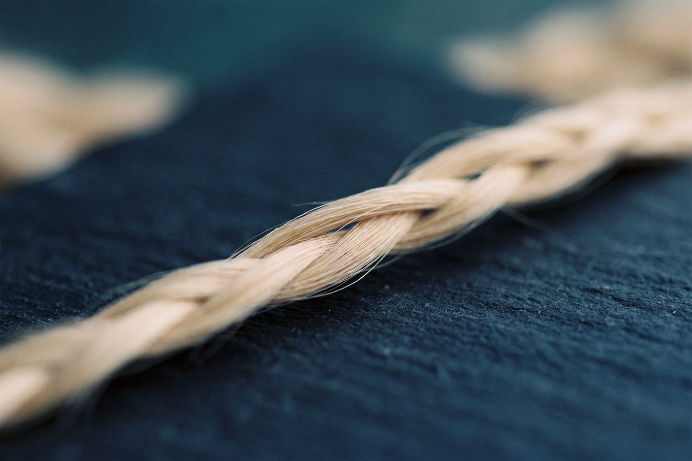 Three fine fibre strands braided into a single cord on navy slate, warm cream rim light