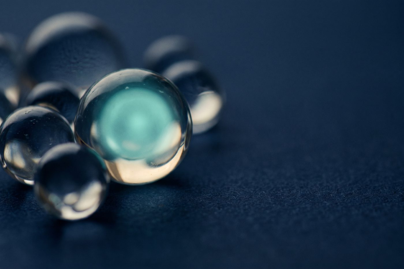 A cluster of clear glass spheres on matte navy, one glowing from within with cool teal light