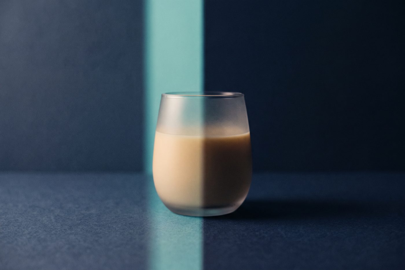 A single glass vessel half in cool teal light and half swallowed by deep navy shadow, the dividing line sharp across the frame