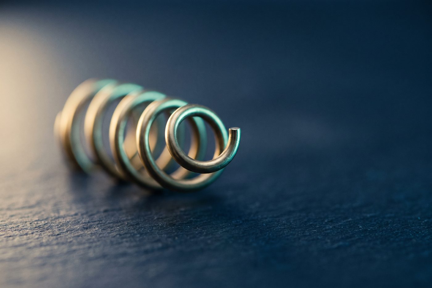 A brass helix rising out of matte navy stone like a growing shoot, extreme macro, teal rim light