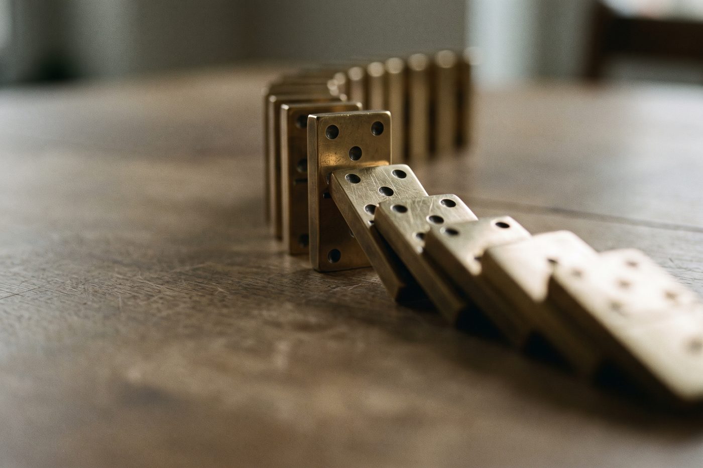 A cascade of brass dominoes caught mid fall on matte navy stone, raking light