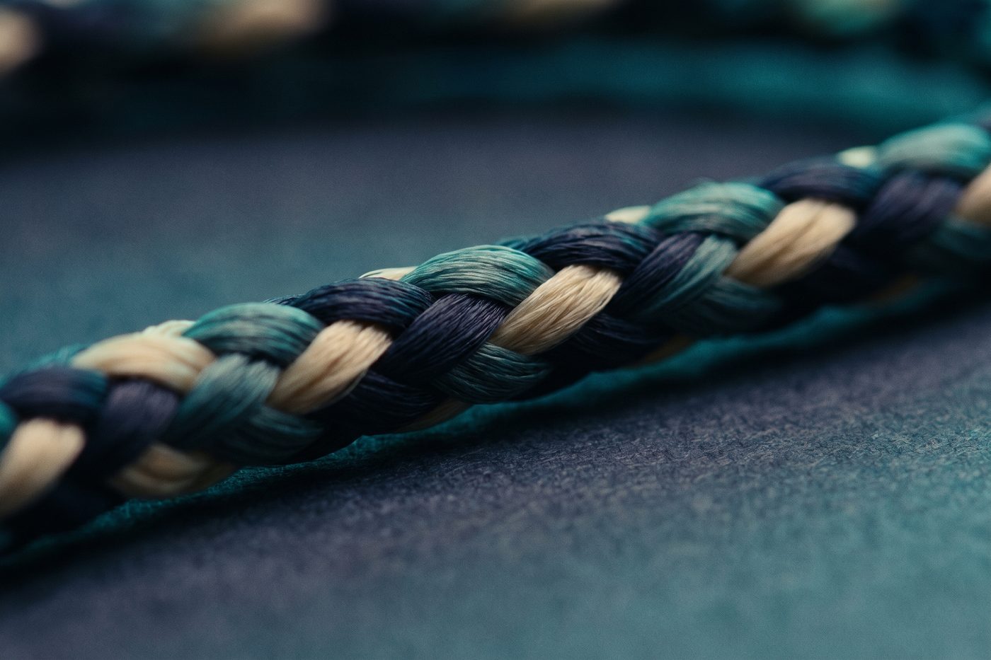 Four fine fibre strands braided into a single cord on navy slate, cool teal rim light