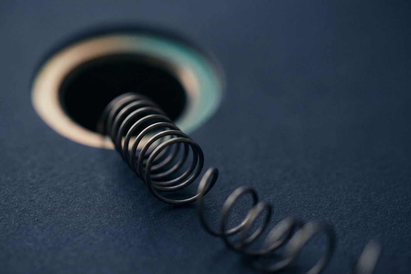 A coiled strand of fine wire emerging from a dark circular aperture, teal rim light, navy
