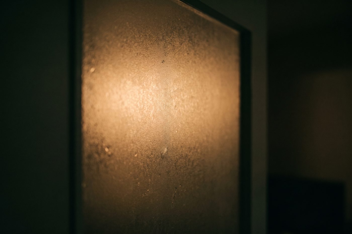 A single warm amber light diffusing through a panel of frosted glass in a dark navy room, extreme macro