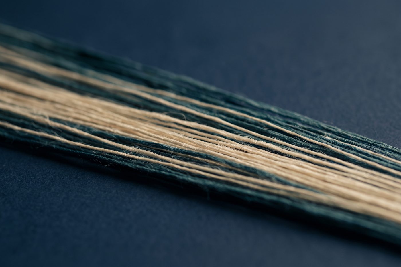 Fine parallel fibres of raw silk under raking teal light on a navy surface, extreme macro