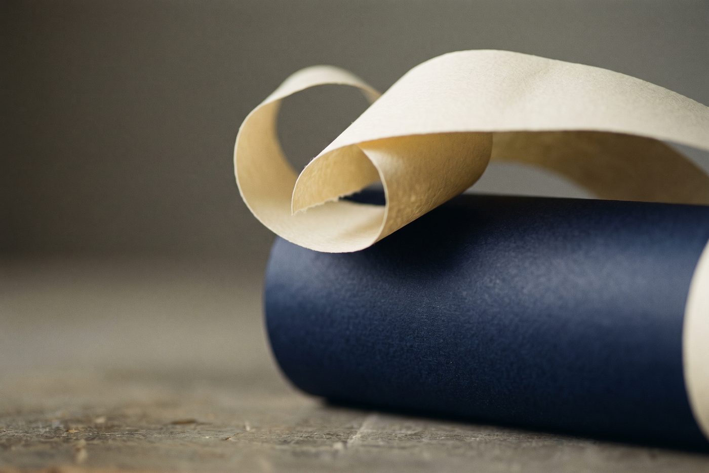 A blank cream label curling away from a matte navy cylinder, raking light