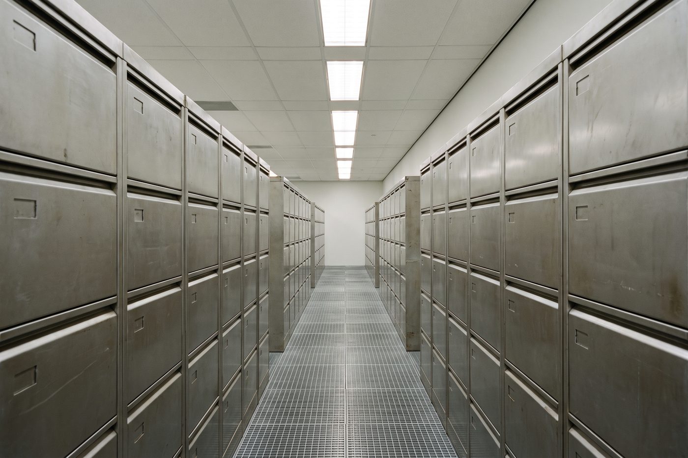 A long corridor of brushed steel filing drawers receding into teal shadow, strictly architectural